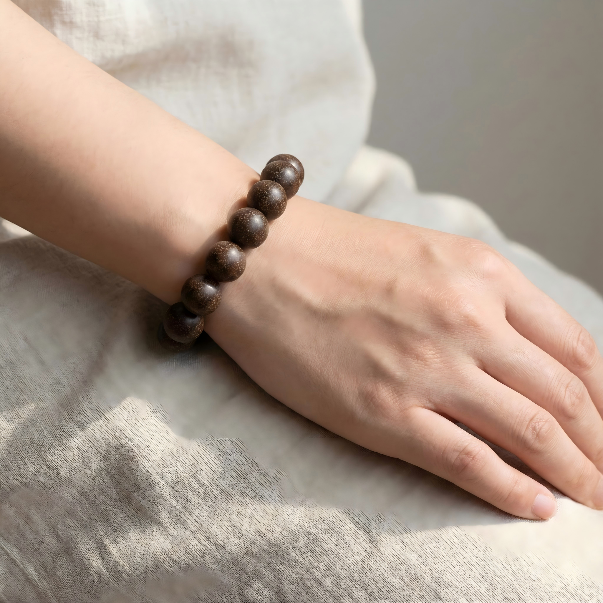 Woman wearing dark agarwood herbal bracelet on wrist with linen clothing for meditation and mindfulness style.