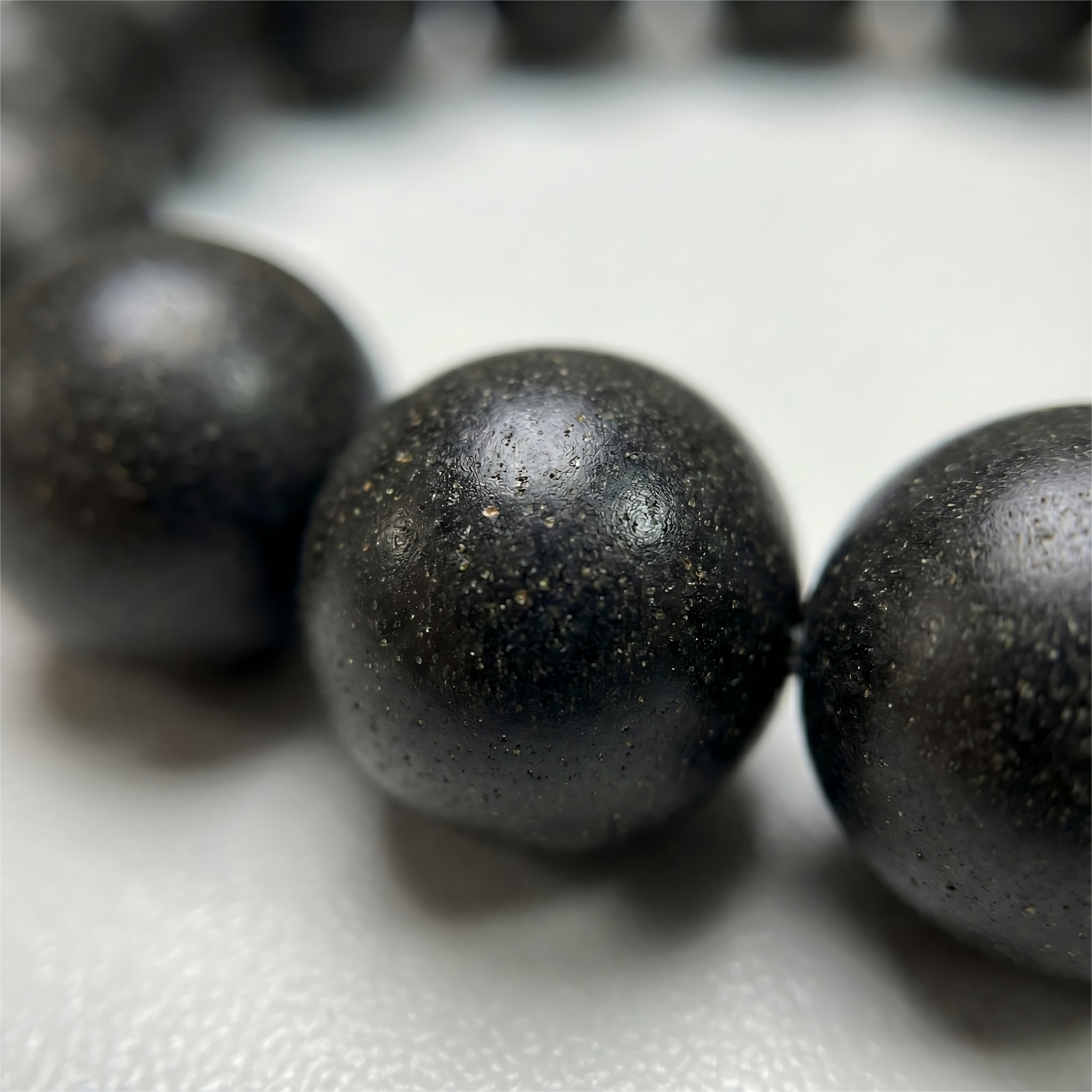 Macro close up of handmade black ambergris clay beads showing natural oily texture and organic grain without glue.