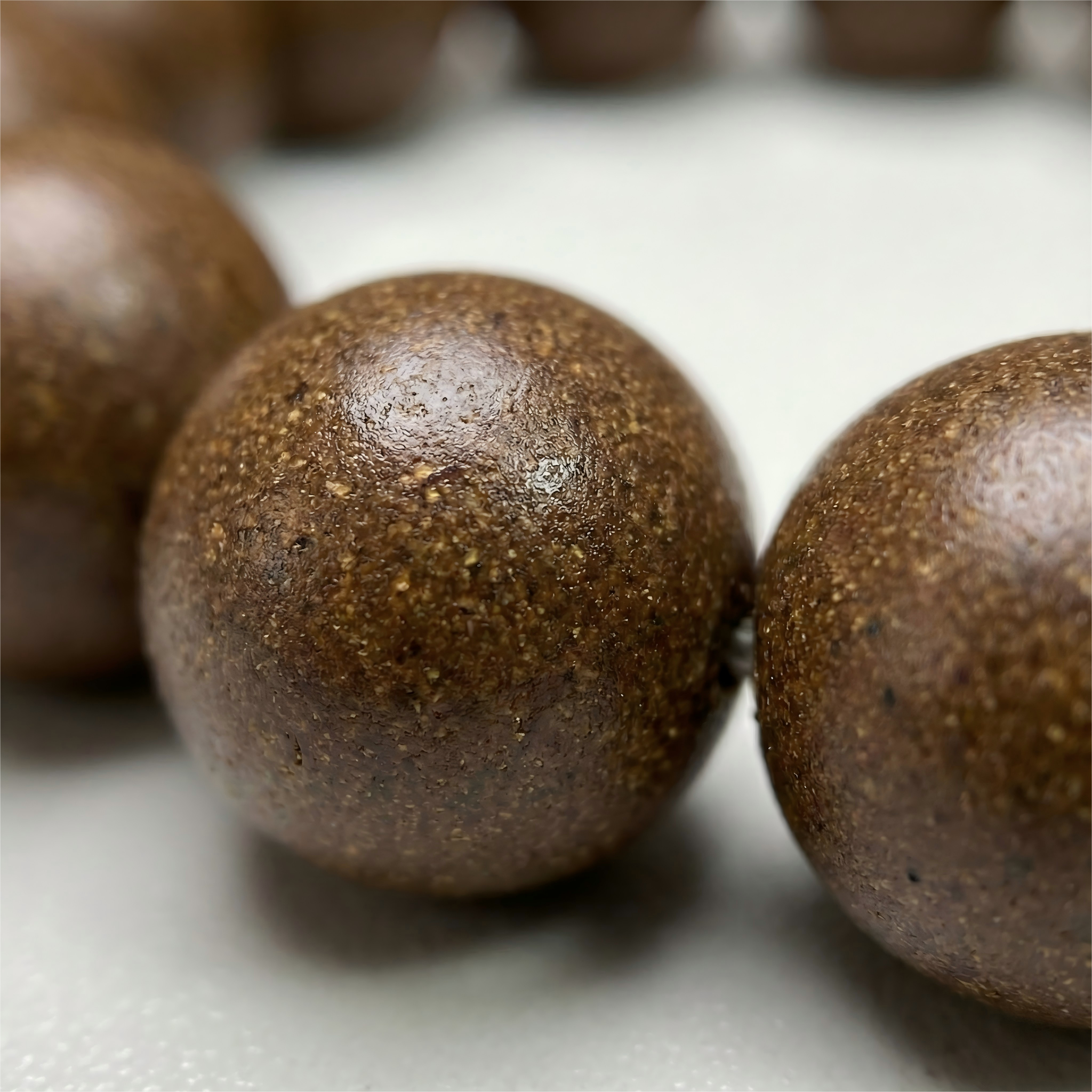 Macro close up of handmade ginseng herbal clay beads showing natural earthy texture and organic grain without chemical glue.