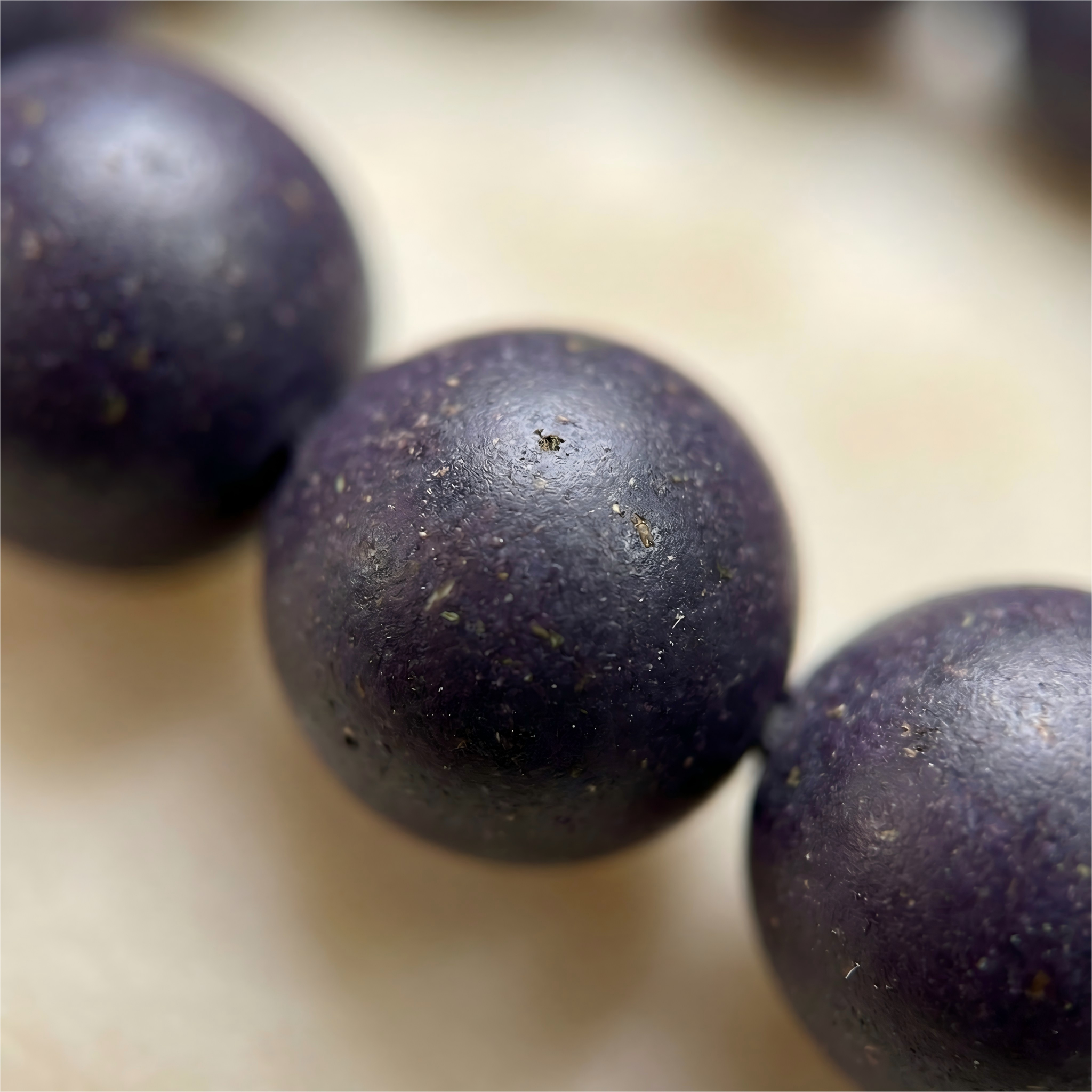 Macro close up of handmade purple Gromwell herbal clay beads showing natural matte texture and organic grain without chemical glue.