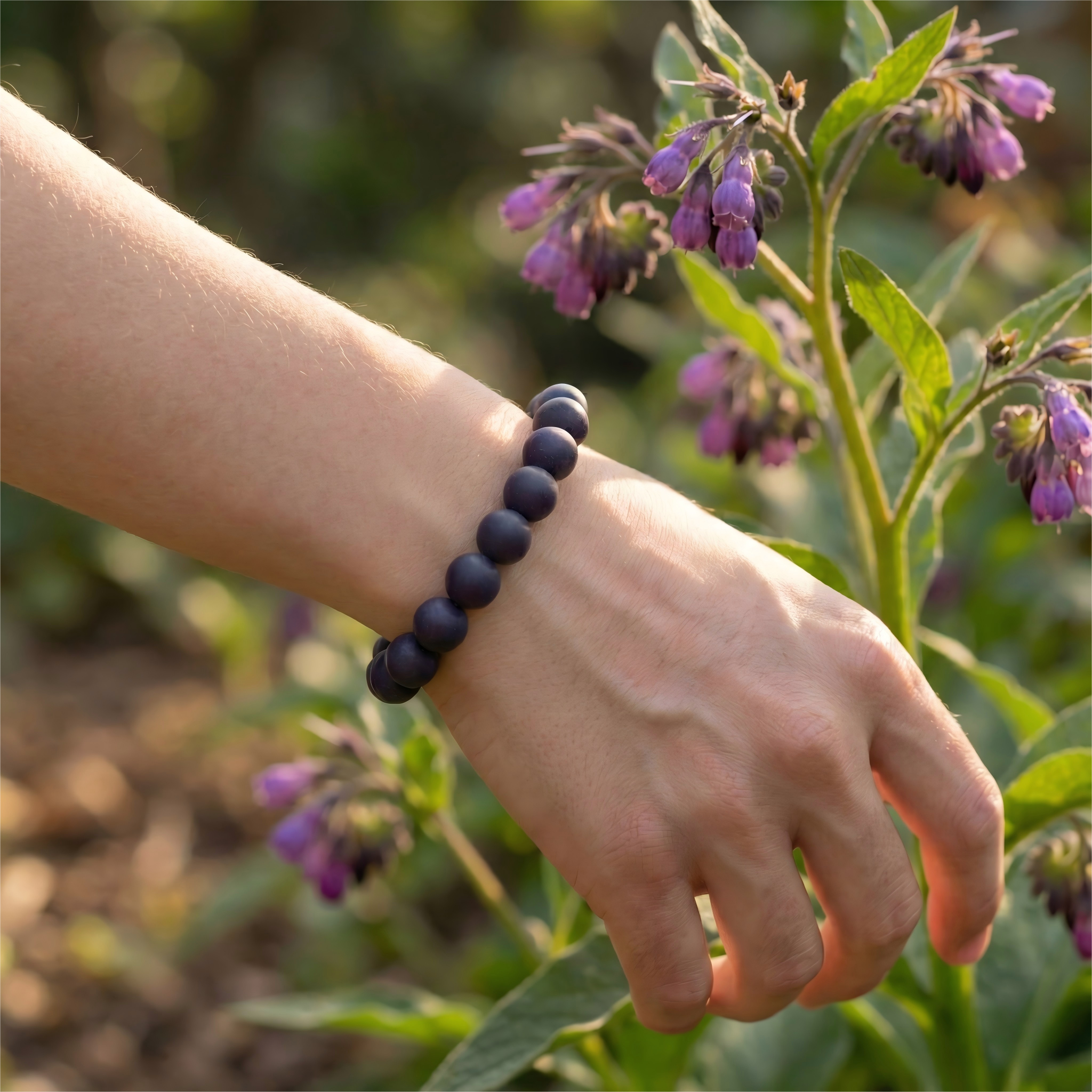 Woman wearing purple Gromwell herbal bracelet on wrist touching purple flowers for nature connection and luck.